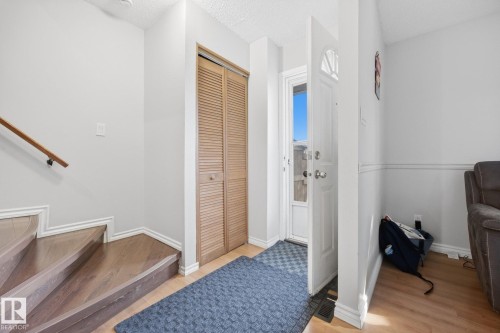 Front entry with wood-finish flooring, louvered bi-fold closet doors, and a wood handrail - #2 14120 80 St Nw, Edmonton, AB 