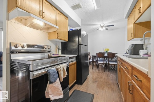 Kitchen featuring a stainless steel range, black refrigerator, wood-finish flooring, and natural wood cabinetry with metal hardware - #2 14120 80 St Nw, Edmonton, AB 
