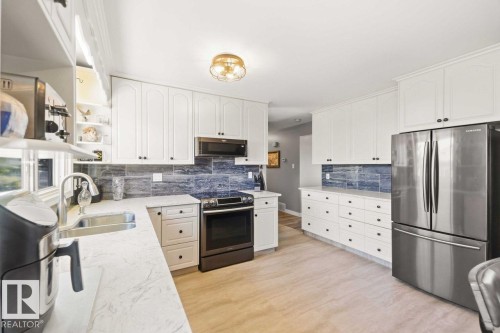 White cabinetry, stainless steel appliances, light-colored countertops, blue-toned tile backsplash, and wood-finish flooring - 13427 83 Street Nw, Edmonton, AB 