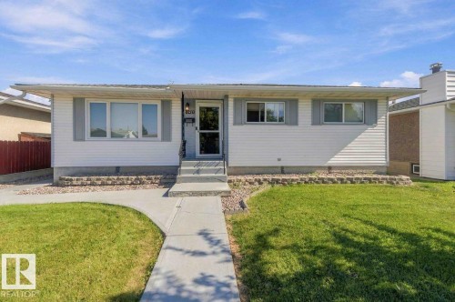White siding exterior with grey window shutters, concrete walkway, and a landscaped front yard with a low retaining wall - 13427 83 Street Nw, Edmonton, AB 