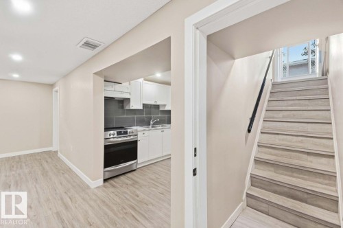 Contemporary kitchen featuring white cabinetry, stainless steel range, gray tile backsplash, and light wood-finish flooring - 13427 83 Street Nw, Edmonton, AB 