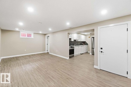 Open-concept living space featuring wood-finish flooring, recessed lighting, and a kitchen with white cabinetry and stainless steel appliances - 13427 83 Street Nw, Edmonton, AB 