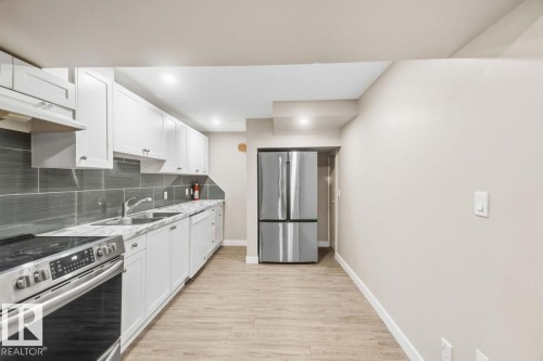 Modern kitchen featuring white cabinetry, gray subway tile backsplash, light-toned wood-finish flooring, stainless steel appliances, and a double-basin sink - 13427 83 Street Nw, Edmonton, AB 