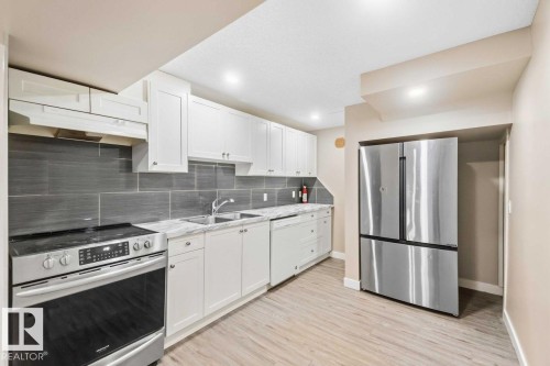 Stainless steel appliances, white cabinetry, grey subway tile backsplash, light wood-finish flooring, and recessed lighting - 13427 83 Street Nw, Edmonton, AB 