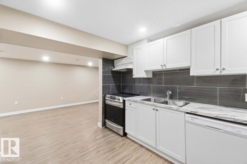 White cabinetry with stainless steel hardware, wood-finish flooring, recessed lighting, and a dark tile backsplash - 13427 83 Street Nw, Edmonton, AB 