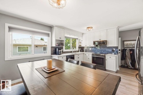 White kitchen cabinetry, stainless steel appliances, wood-finish flooring, and a subway tile backsplash - 13427 83 Street Nw, Edmonton, AB 