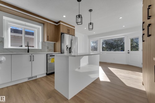 Modern kitchen featuring white and wood-finish cabinetry, a large center island, wood-finish flooring, and stainless steel appliances - 3320 43 Street Nw, Edmonton, AB 