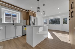 Modern kitchen featuring white and wood-finish cabinetry, a large center island, wood-finish flooring, and stainless steel appliances - 
