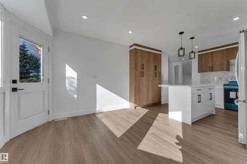 White shaker style door with transom window, recessed lighting, wood-finish flooring, white kitchen island with black hardware, and wood-tone cabinetry - 3320 43 Street Nw, Edmonton, AB 