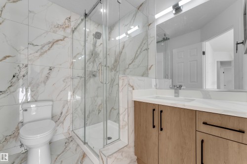 Glass-enclosed shower, wood-finish vanity with ample storage, integrated sink, and large wall-mounted mirror with overhead lighting - 3320 43 Street Nw, Edmonton, AB 