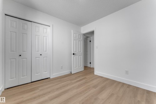 Wood-finish flooring, white walls, white bi-fold closet doors, and contrasting dark hardware - 3320 43 Street Nw, Edmonton, AB 