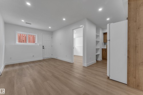 Light wood-finish flooring, recessed ceiling lights, built-in shelving, white walls, and a contemporary white door - 3320 43 Street Nw, Edmonton, AB 