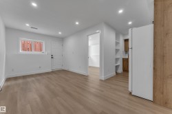 Light wood-finish flooring, recessed ceiling lights, built-in shelving, white walls, and a contemporary white door - 