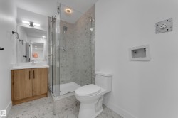 Glass-enclosed shower with a recessed light, wood-finish vanity with a white countertop, and a wall-mounted mirror with integrated lighting - 