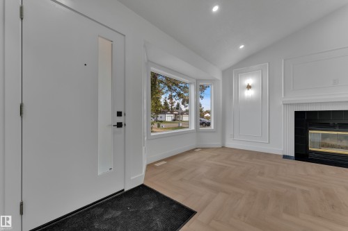 Vaulted ceiling, herringbone wood-finish flooring, bay windows, contemporary fireplace with black tile surround, and decorative wall molding with sconce lighting - 3320 43 Street Nw, Edmonton, AB 