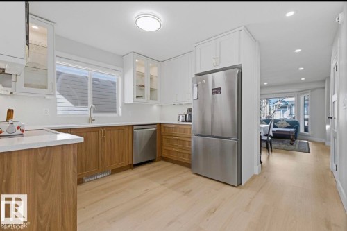 Modern kitchen featuring light wood-finish flooring, white upper cabinetry with glass-front accents, wood-finish lower cabinetry, and stainless steel appliances - 3830 22 Street Nw, Edmonton, AB 