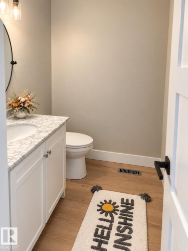 White vanity with a light-toned countertop, a round mirror, and wood-finish flooring - 3830 22 Street Nw, Edmonton, AB 