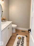White vanity with a light-toned countertop, a round mirror, and wood-finish flooring - 