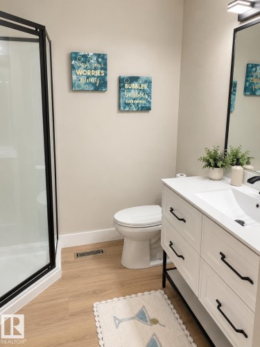 Corner shower with black frame, light wood-finish flooring, white vanity with black hardware, integrated sink, and wall-mounted light fixture - 3830 22 Street Nw, Edmonton, AB 