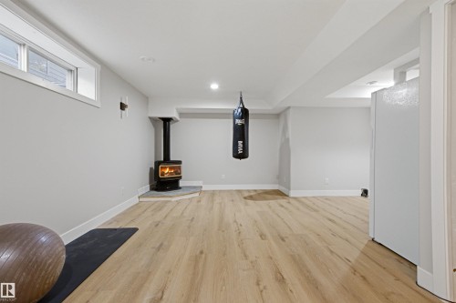 Spacious lower level featuring light wood-finish flooring, a wood-burning stove with a stone hearth, and recessed lighting - 3830 22 Street Nw, Edmonton, AB 
