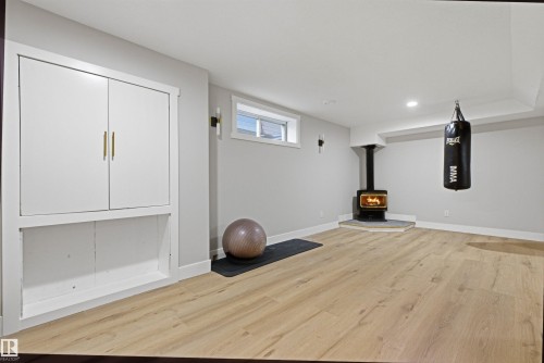 Wood-finish flooring throughout, featuring a corner-set wood-burning stove on a stone hearth, built-in cabinetry with gold-tone hardware, recessed lighting, and a horizontal window - 3830 22 Street Nw, Edmonton, AB 