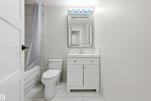 White vanity with integrated sink, chrome faucet, framed mirror, and overhead vanity lighting - 3830 22 Street Nw, Edmonton, AB 