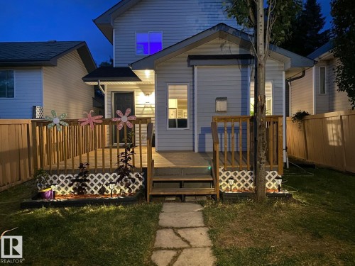 Two-story exterior with light-colored siding, a privacy fence, a wood deck with railing, and a stone-paved path - 3830 22 Street Nw, Edmonton, AB 