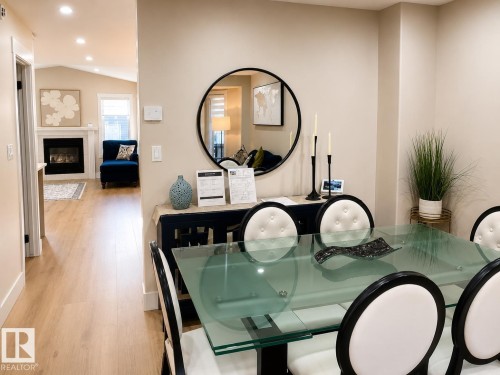 Glass-top dining table with upholstered chairs, wood-finish flooring, recessed lighting, and a built-in fireplace with a mantel - 3830 22 Street Nw, Edmonton, AB 
