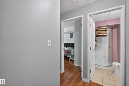Wood-finish flooring leading to a full bathroom featuring a white toilet, enclosed shower, and ceramic tile flooring - 333 Kirkpatrick Crescent Nw, Edmonton, AB 