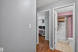 Wood-finish flooring leading to a full bathroom featuring a white toilet, enclosed shower, and ceramic tile flooring - 