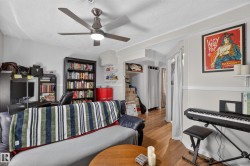 Hardwood-finish flooring, ceiling fan with integrated lighting, built-in shelving, and a doorway opening to an additional space - 