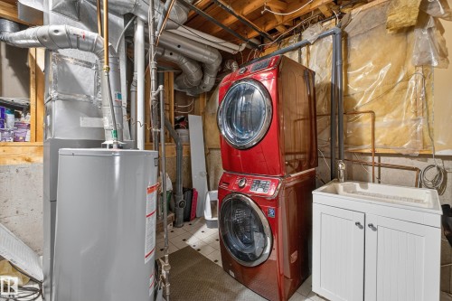 Red stackable washer and dryer, laundry sink with white cabinetry, and water heater - 333 Kirkpatrick Crescent Nw, Edmonton, AB 