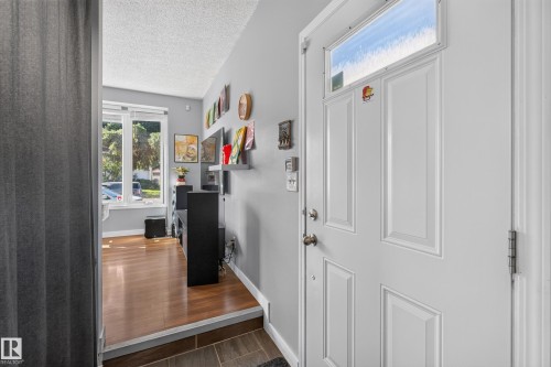 Entry with a paneled door featuring a transom window, leading to a living area with wood-finish flooring and large windows - 333 Kirkpatrick Crescent Nw, Edmonton, AB 