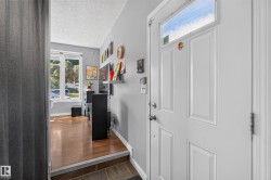Entry with a paneled door featuring a transom window, leading to a living area with wood-finish flooring and large windows - 