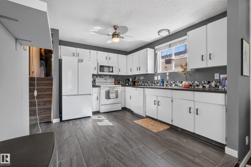 Kitchen featuring white cabinetry, dark countertops, tiled backsplash, and wood-finish flooring - 333 Kirkpatrick Crescent Nw, Edmonton, AB 