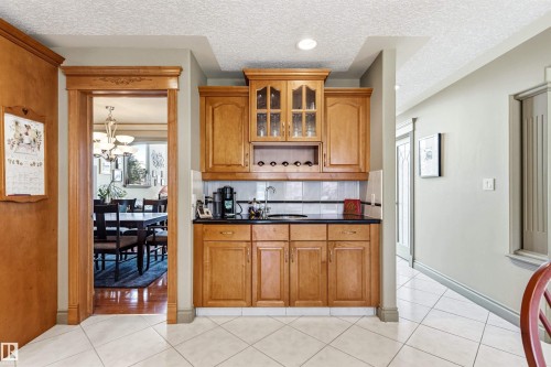 Built-in wet bar featuring wood cabinetry, integrated wine storage, a black countertop, and a tile backsplash - 703 107A Street Sw, Edmonton, AB 
