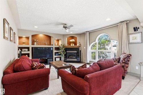 Living room featuring a gas fireplace with mantel, built-in recessed shelving, an arched window, and recessed ceiling lighting - 703 107A Street Sw, Edmonton, AB 