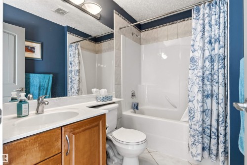 Bathroom featuring a wood-finish vanity with an integrated sink, a large wall-mounted mirror, and overhead vanity lighting - 703 107A Street Sw, Edmonton, AB 