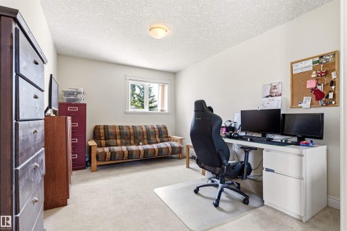 Carpeted room featuring a white window with exterior tree views, a ceiling-mounted light fixture, and neutral-toned walls - 703 107A Street Sw, Edmonton, AB 