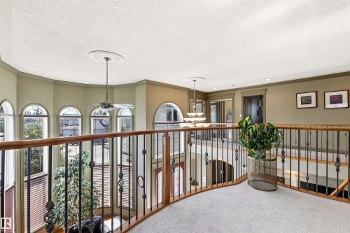 Upper-level landing featuring light-toned carpeting, a wood and wrought-iron railing, and arched windows - 703 107A Street Sw, Edmonton, AB 