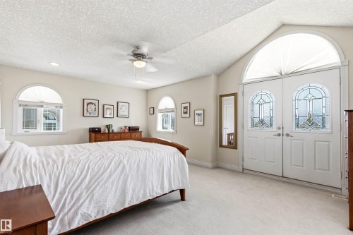 Vaulted ceiling bedroom featuring arched double entry doors with decorative glass panels, a ceiling fan, recessed lighting, and arched windows with blinds - 703 107A Street Sw, Edmonton, AB 