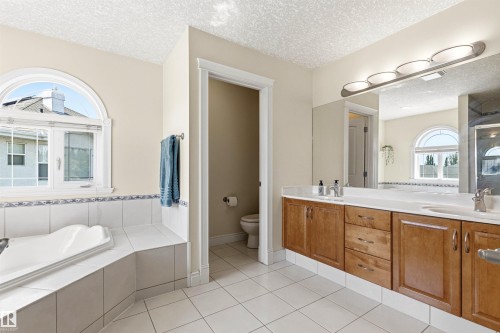 Bathroom featuring a large vanity with dual sinks, wood-finish cabinetry, and a full-width mirror - 703 107A Street Sw, Edmonton, AB 