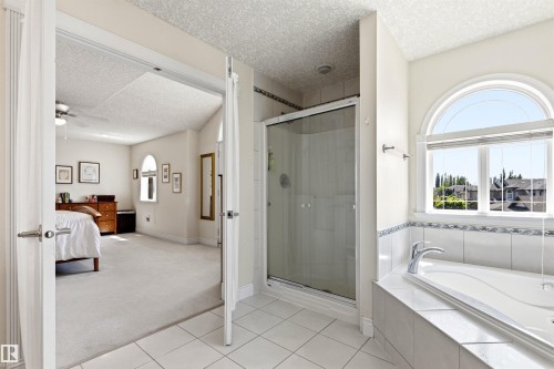 Bathroom featuring a tiled soaking tub with an arched window, a glass-enclosed shower, and tile flooring - 703 107A Street Sw, Edmonton, AB 
