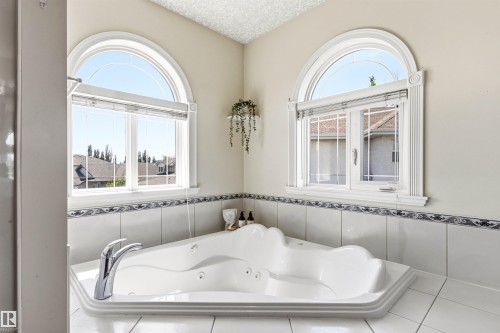 Corner jetted tub featuring dual chrome fixtures and white tile surround with decorative trim - 703 107A Street Sw, Edmonton, AB 