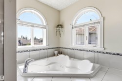 Corner jetted tub featuring dual chrome fixtures and white tile surround with decorative trim - 
