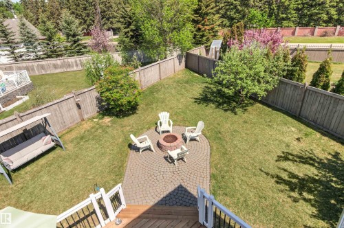 Expansive backyard featuring a circular paver patio with a built-in fire pit, surrounded by a manicured lawn and mature trees - 703 107A Street Sw, Edmonton, AB 