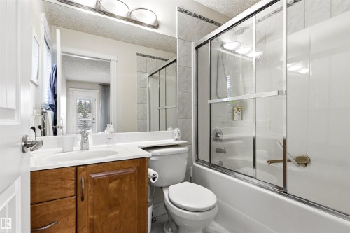 Bathroom featuring a wood-finish vanity with an integrated sink, a large mirror, and an overhead light fixture - 703 107A Street Sw, Edmonton, AB 