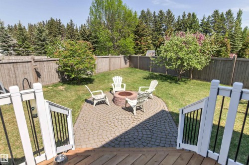Expansive backyard featuring a circular paver patio with a built-in fire pit, surrounded by lush green lawn and mature trees - 703 107A Street Sw, Edmonton, AB 