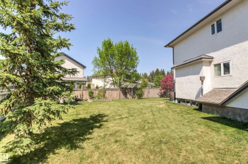 Expansive backyard featuring a manicured lawn, established landscaping, mature trees, and a wooden perimeter fence - 703 107A Street Sw, Edmonton, AB 