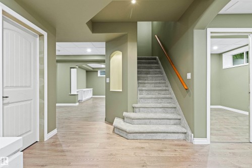 Carpeted staircase with wood handrail, wood-finish flooring, recessed lighting, and wall niche - 703 107A Street Sw, Edmonton, AB 